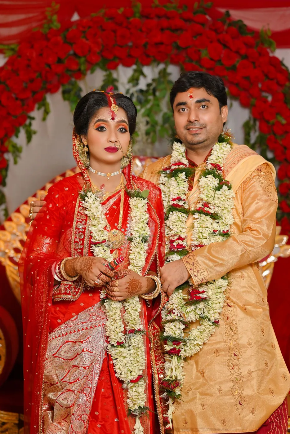 An Indian bride and groom with flower garlands in front of a red floral backdrop